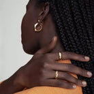 NYLD Glamour Collection by NEWYORKLISTED: Close-up of a person wearing gold hoop earrings and rings on a neutral background