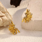 NYLD Glamour Collection by NEWYORKLISTED: Gold leaf-shaped earrings with rhinestones on a textured beige surface