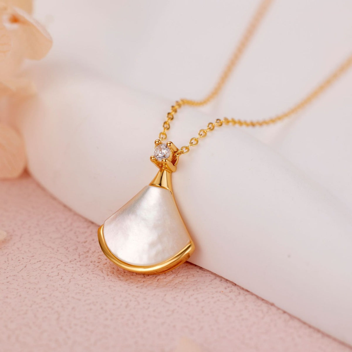 NYLD Glamour By NEWYORKLISTED: Gold necklace with a white pendant on a soft pink background