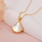 NYLD Glamour By NEWYORKLISTED: Gold necklace with a white pendant on a soft pink background