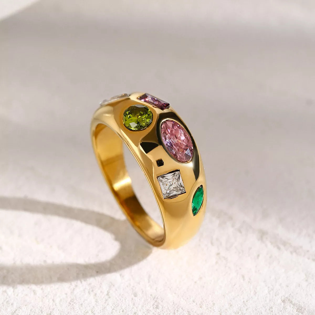 NYLD Glamour Collection by NEWYORKLISTED: Gold ring with multicolored gemstones on a textured white surface