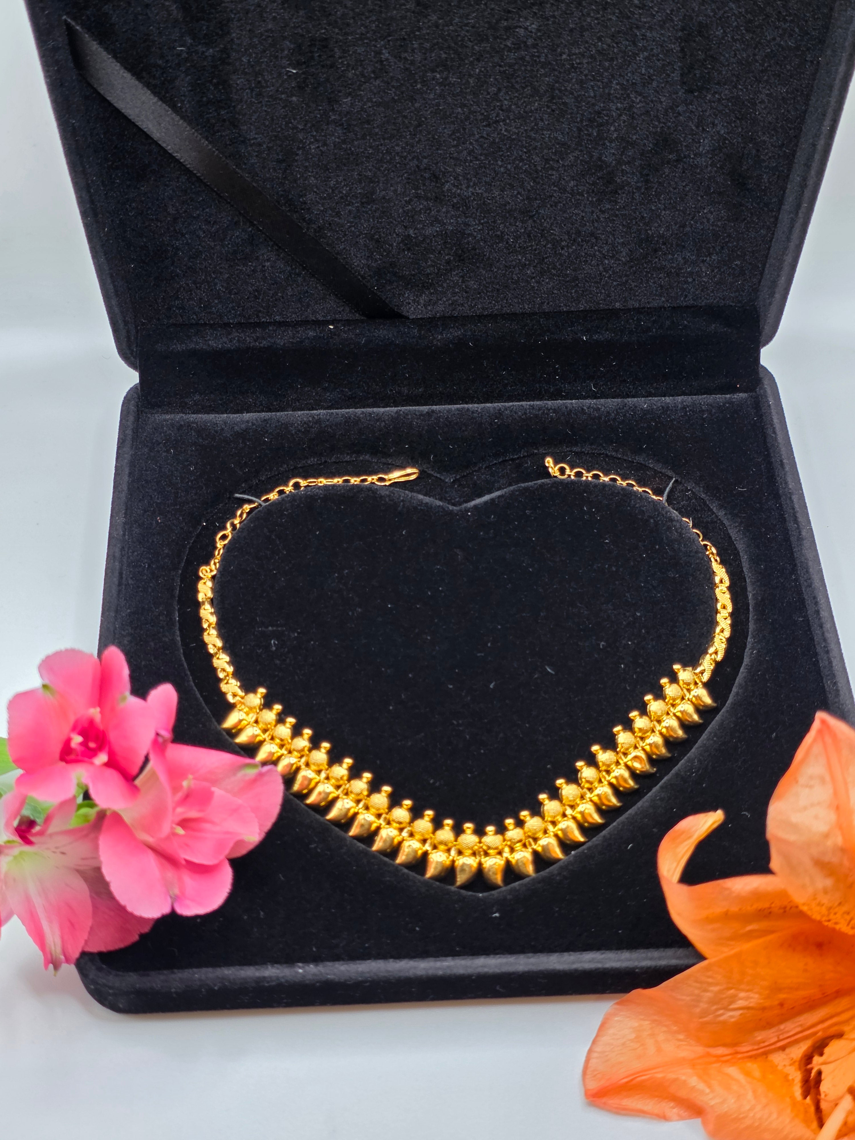 NEWYORKLISTED: 22k Gold necklace in a black jewelry box with flowers on a light background