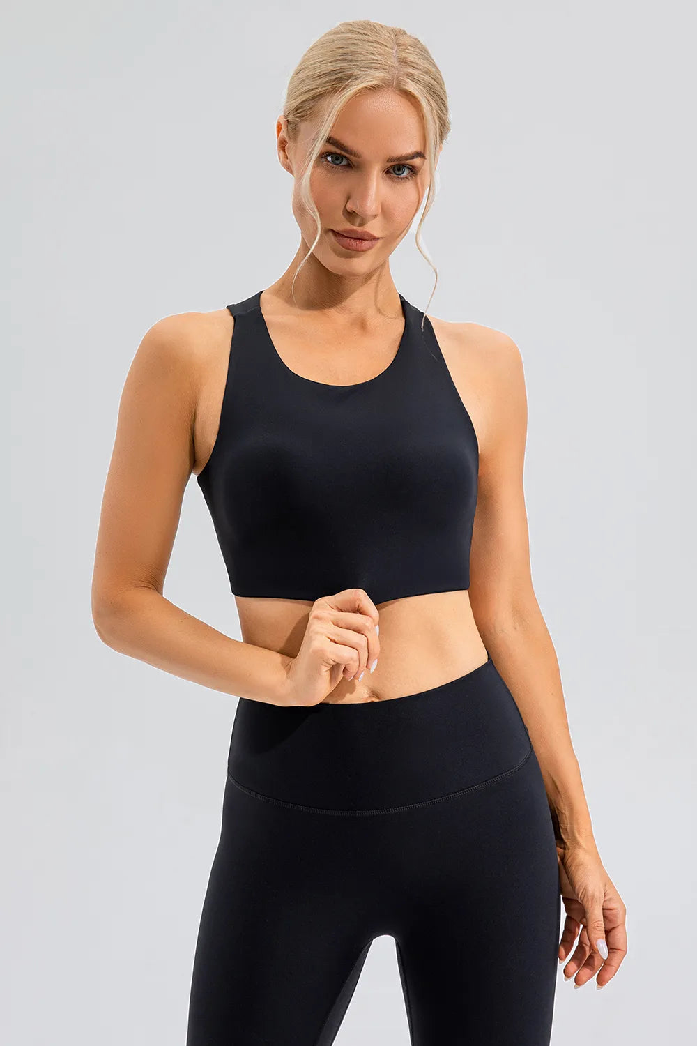 NEWYORKLISTED ACTIVEWEAR COLLECTION: Woman wearing a black sports bra and leggings on a gray background