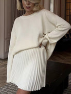 NEWYORKLISTED STYLE COLLECTION: Person wearing a cream sweater and white pleated skirt indoors.