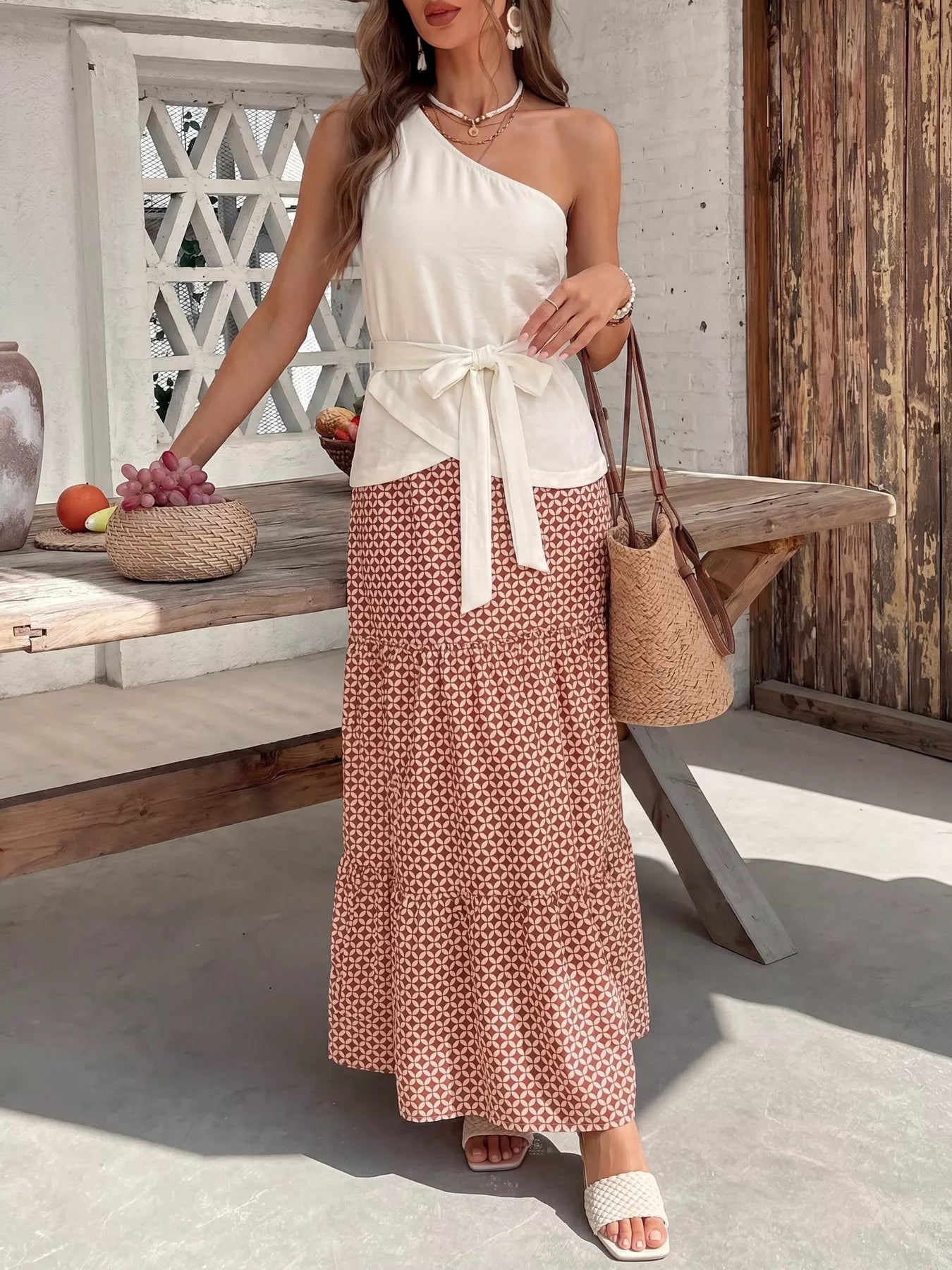 NEWYORKLISTED STYLE COLLECTION: Woman in a white top and patterned skirt holding a woven bag outdoors.