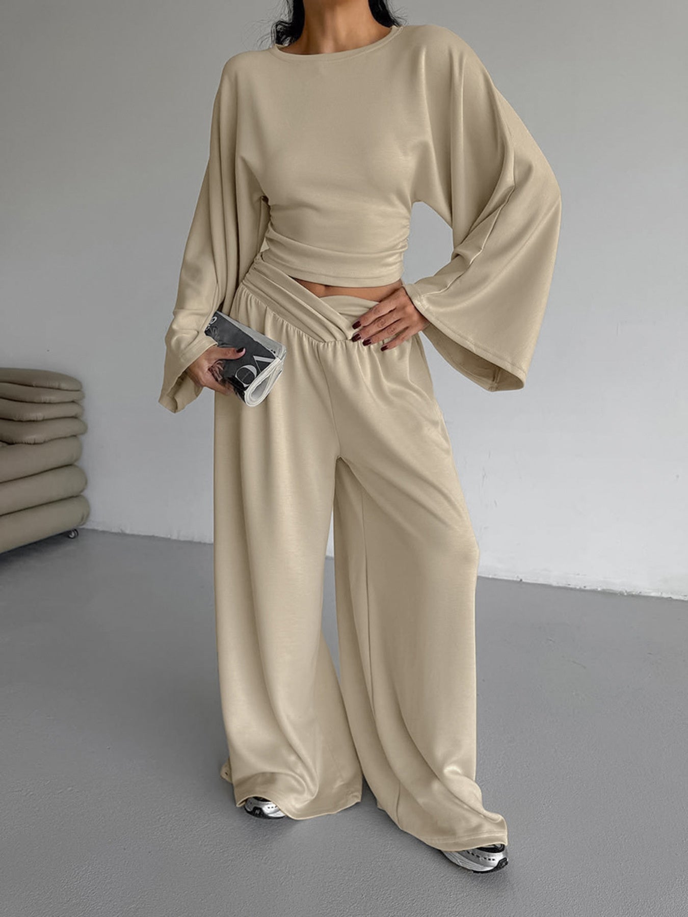 NEWYORKLISTED STYLE COLLECTION: Person wearing a beige outfit with wide sleeves and pants, holding a phone.