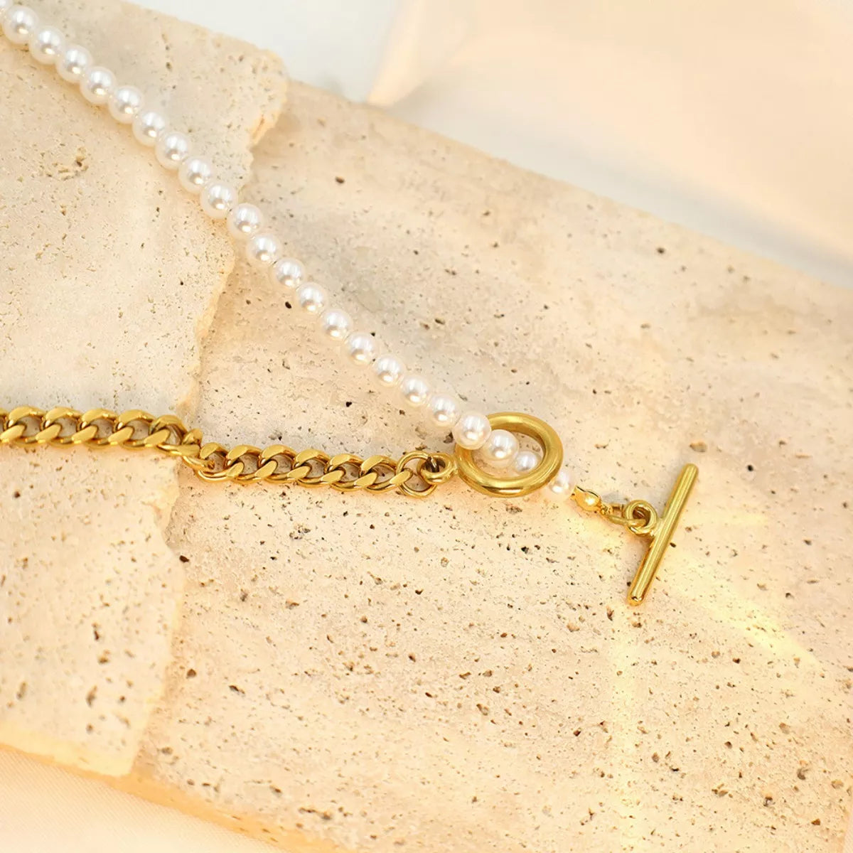 Gold bracelet with a pearl charm on a beige stone surface