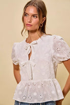 NEWYORKLISTED STYLE COLLECTION:  Woman wearing a white lace blouse with puff sleeves against a beige background