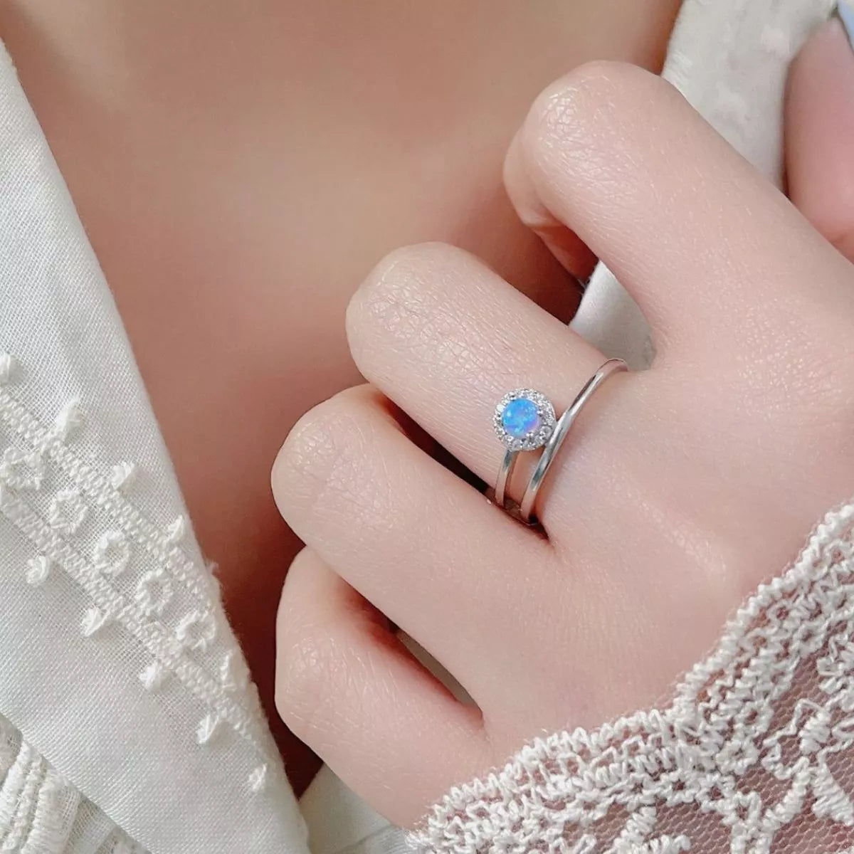 NYLD Glamour Collection by NEWYORKLISTED: Close-up of a hand wearing a silver ring with a blue gemstone, against a soft background.