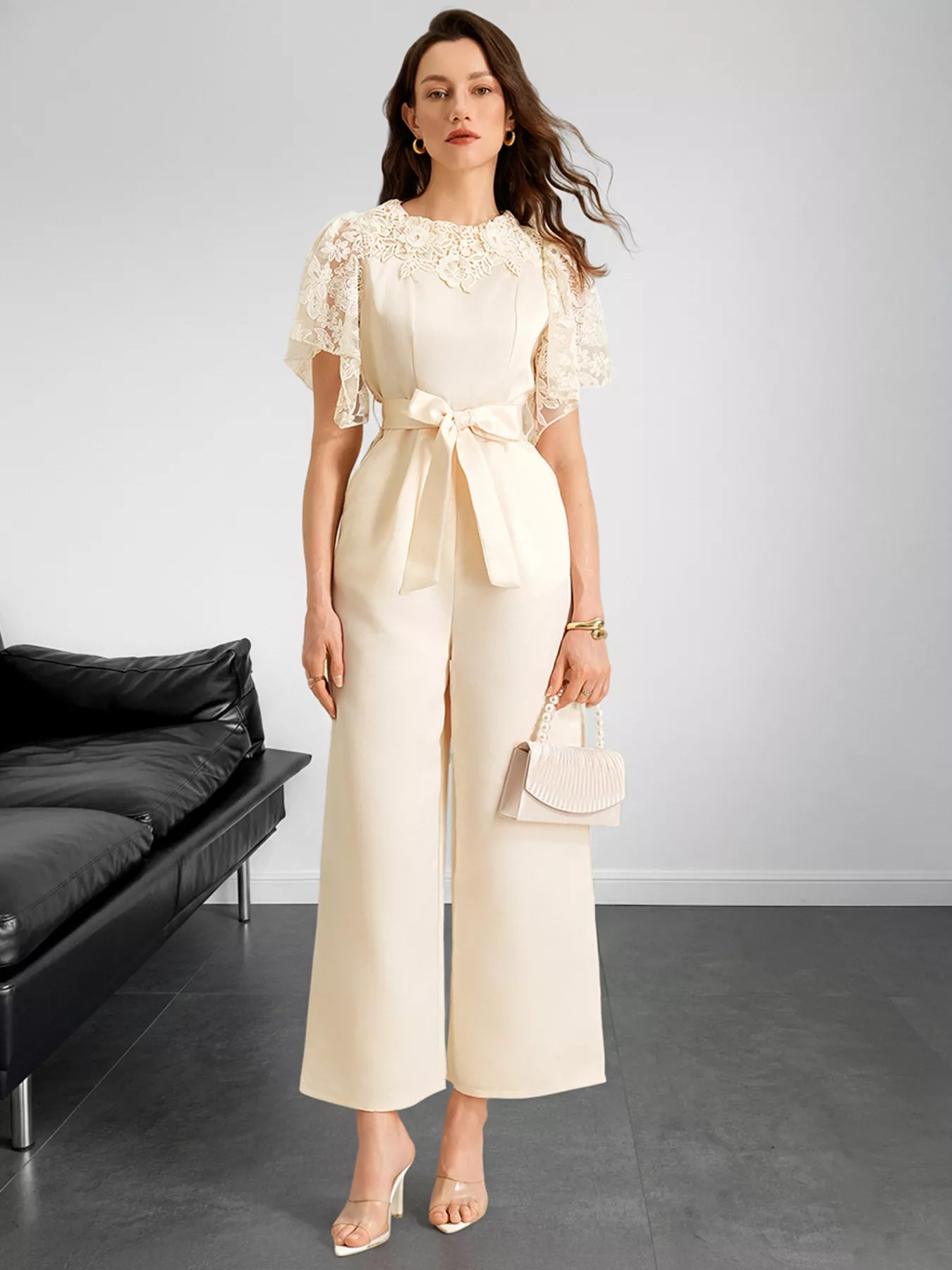 NEWYORKLISTED STYLE COLLECTION: Woman in a cream lace top and wide-leg pants holding a handbag against a plain background