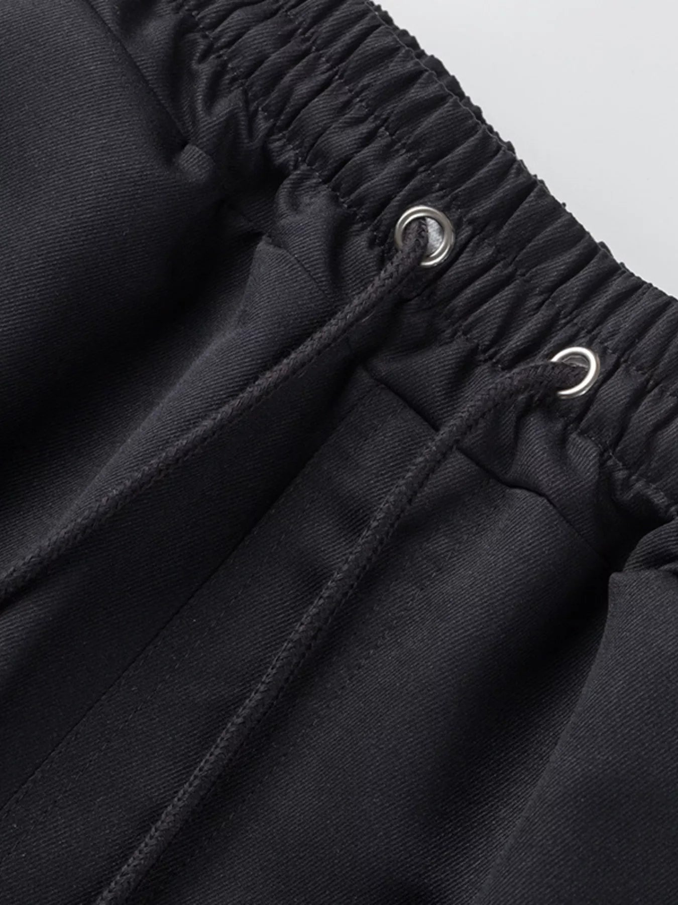 NEWYORKLISTED ATLAS MEN'S COLLECTION: Close-up of black pants with drawstring waistband on a light gray background