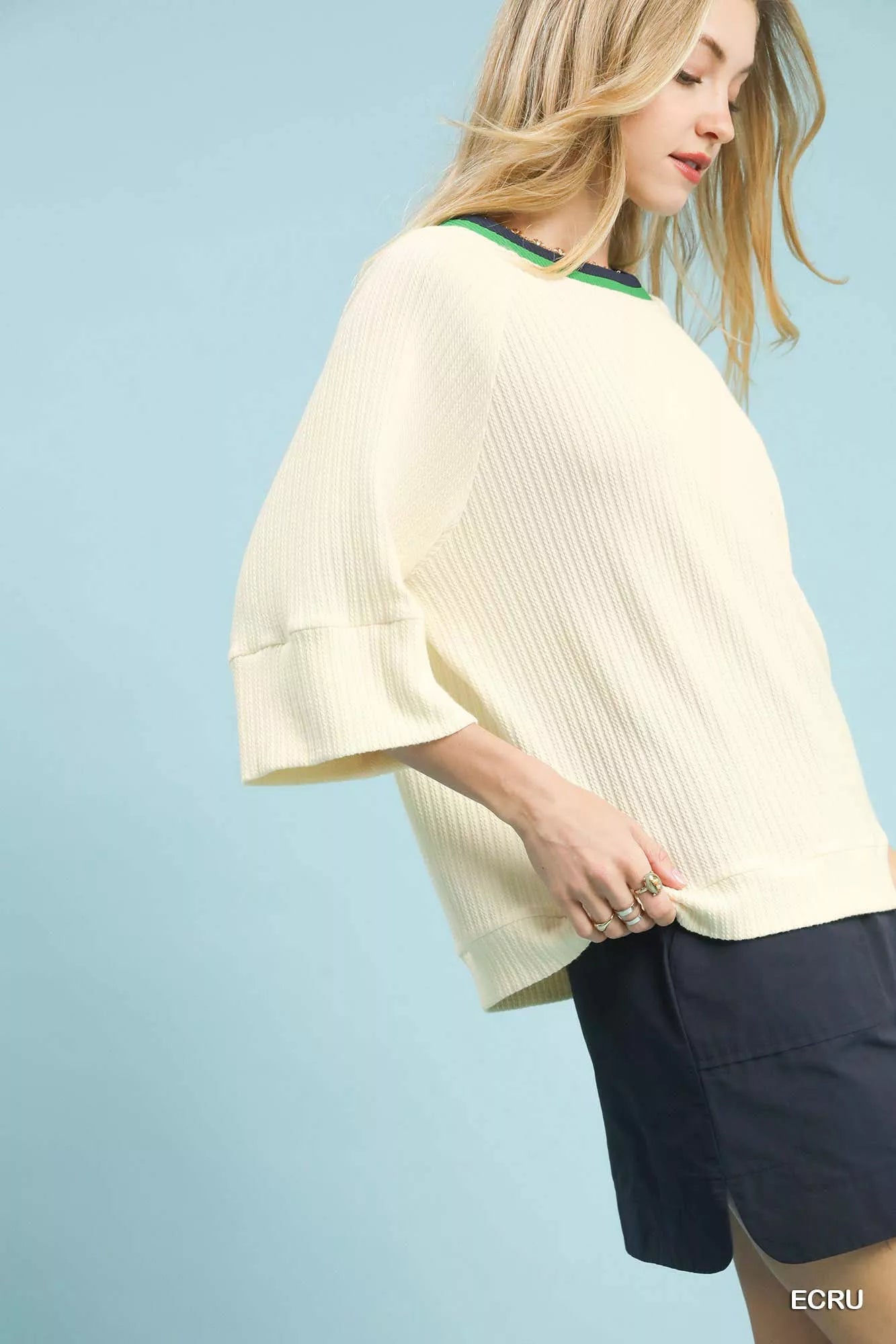 NEWYORKLISTED STYLE COLLECTION: Woman wearing a light-colored top and dark shorts against a light blue background