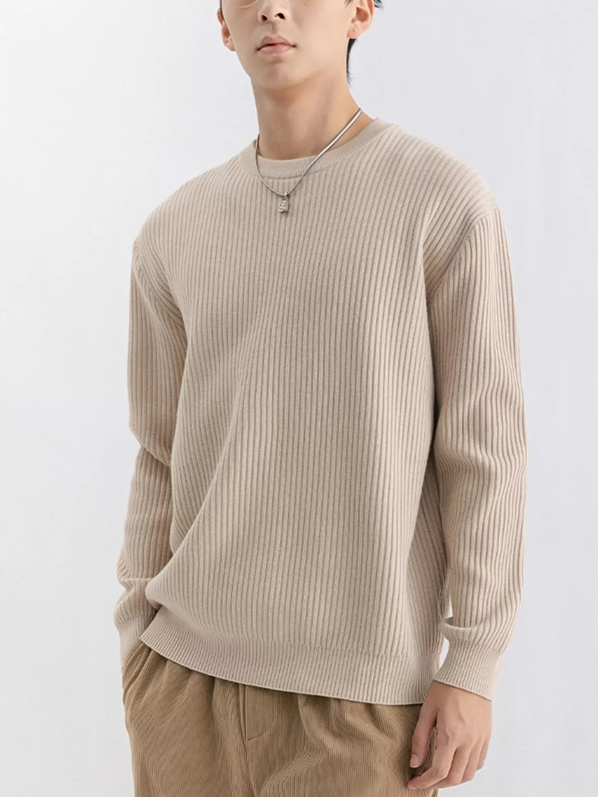 NEWYORKLISTED ATLAS MEN'S COLLECTION: A man wearing a beige ribbed long-sleeve crewneck sweater and tan pants, photographed against a clean light gray studio background.