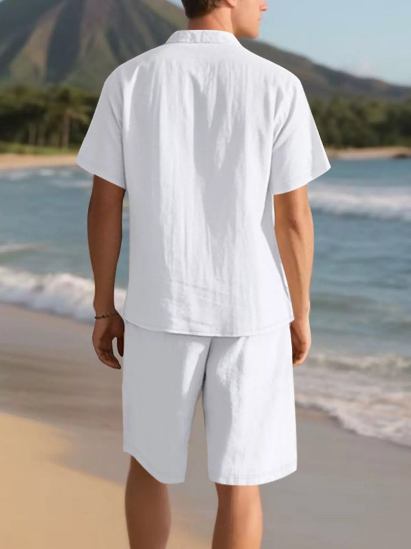 NEWYORKLISTED ATLAS MEN'S COLLECTION: Person wearing a white shirt and shorts on a beach with mountains in the background
