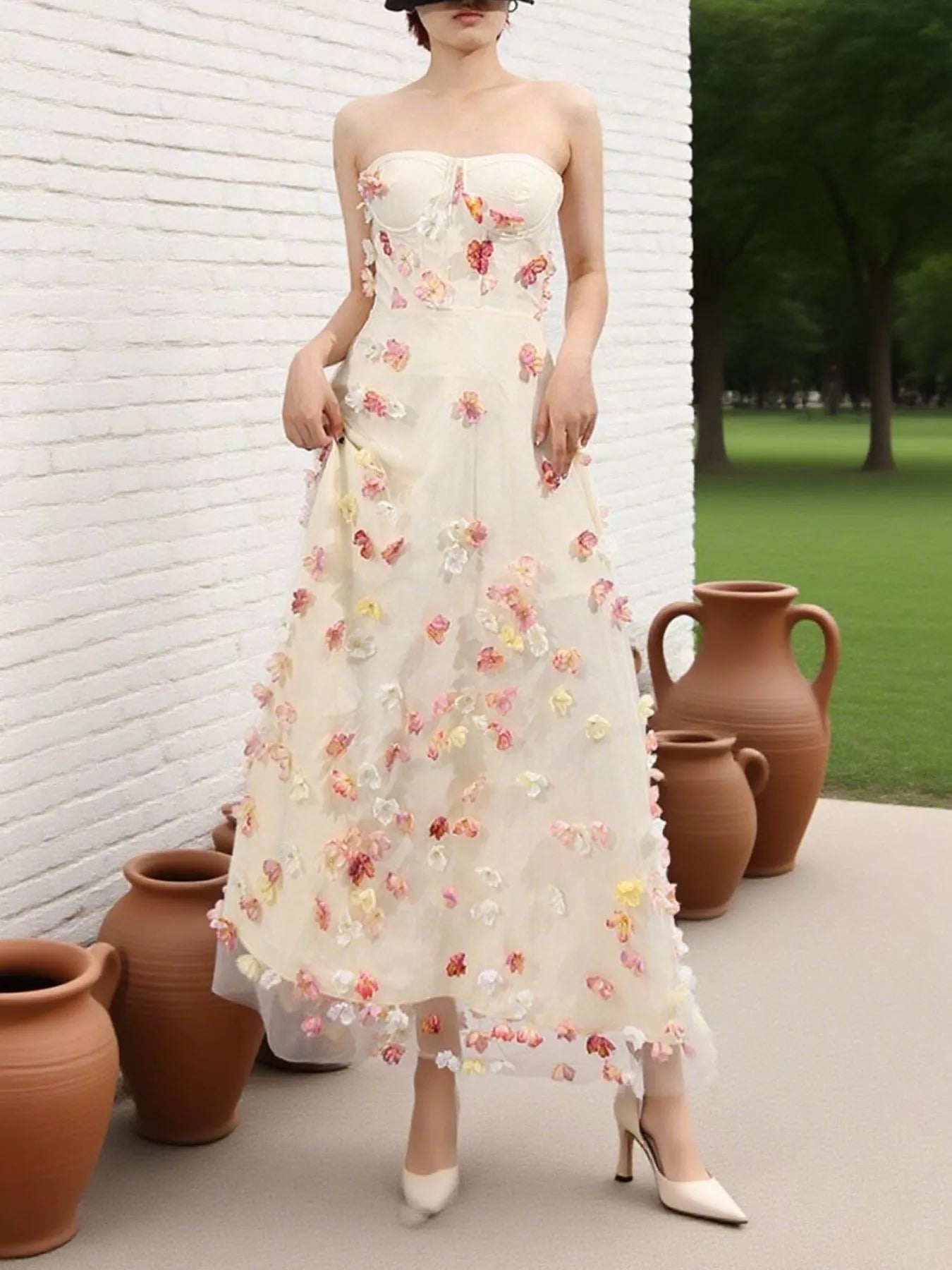 NEWYORKLISTED STYLE COLLECTION: Woman wearing a strapless floral dress standing next to terracotta pots against a white brick wall.