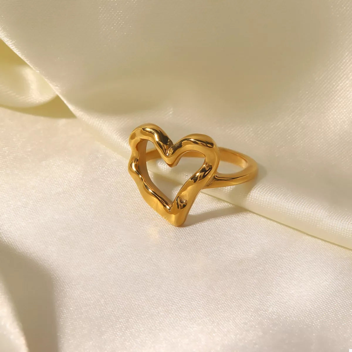 NYLD Glamour Collection by NEWYORKLISTED: Gold heart-shaped ring on a soft beige fabric background