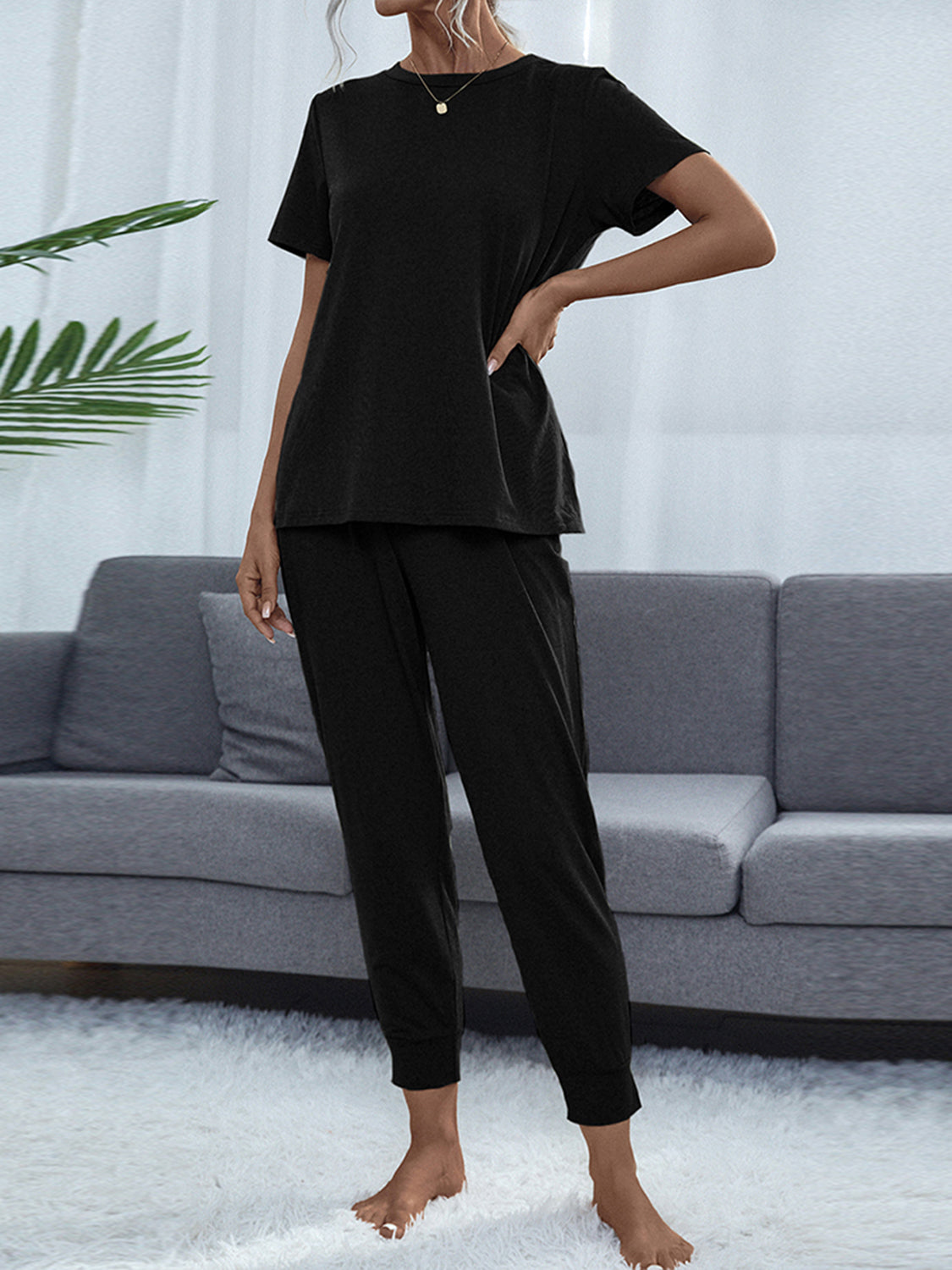 NEWYORKLISTED Intimate Apparel: Person wearing a black outfit standing in a living room with a gray sofa and white walls.