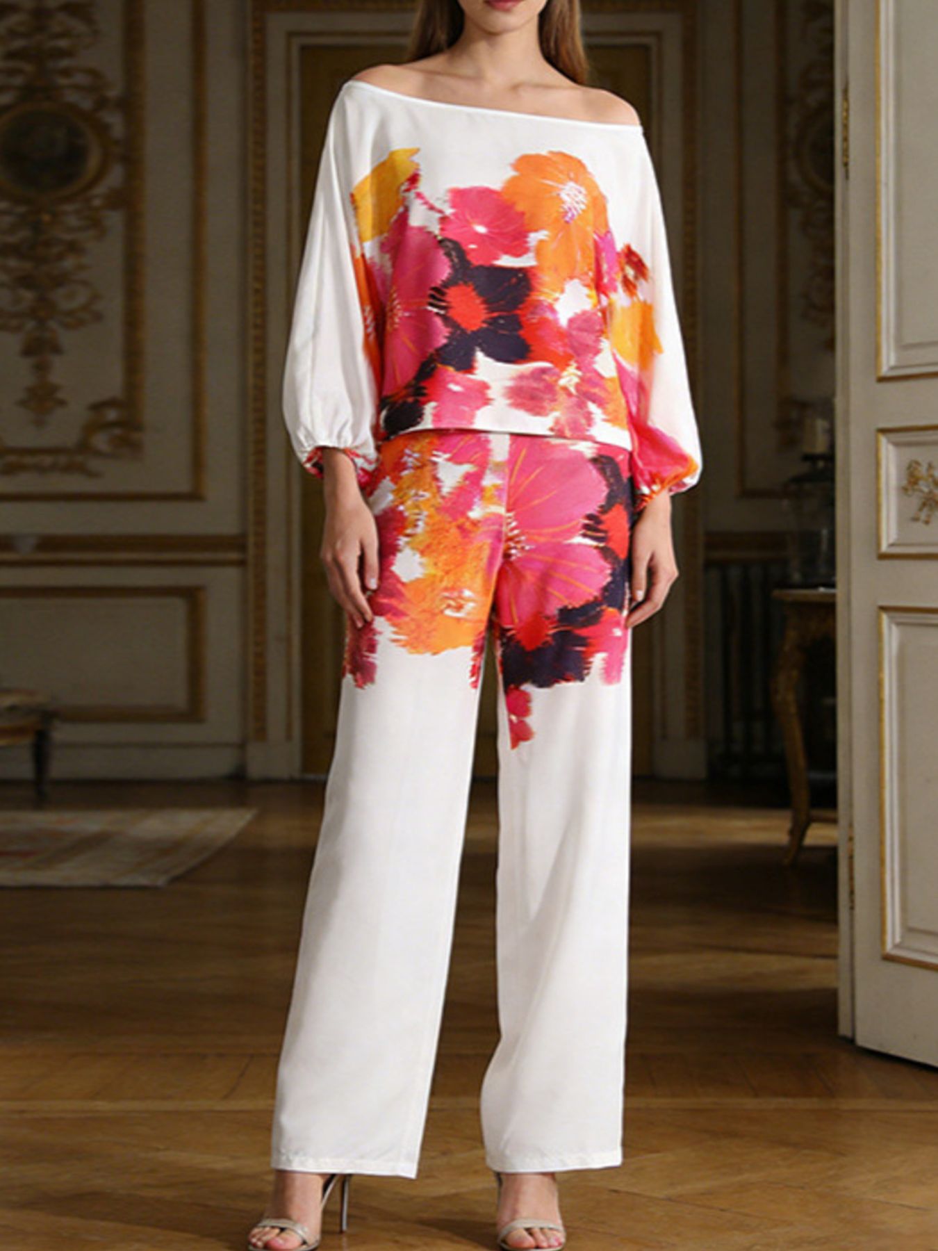 NEWYORKLSITED STYLE COLLECTION: Woman wearing a colorful floral off-shoulder top and white pants in an elegant room.