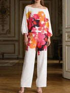NEWYORKLSITED STYLE COLLECTION: Woman wearing a colorful floral off-shoulder top and white pants in an elegant room.