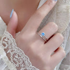 NYLD Glamour Collection by NEWYORKLISTED: Hand wearing a silver ring with a blue gemstone on a lace background