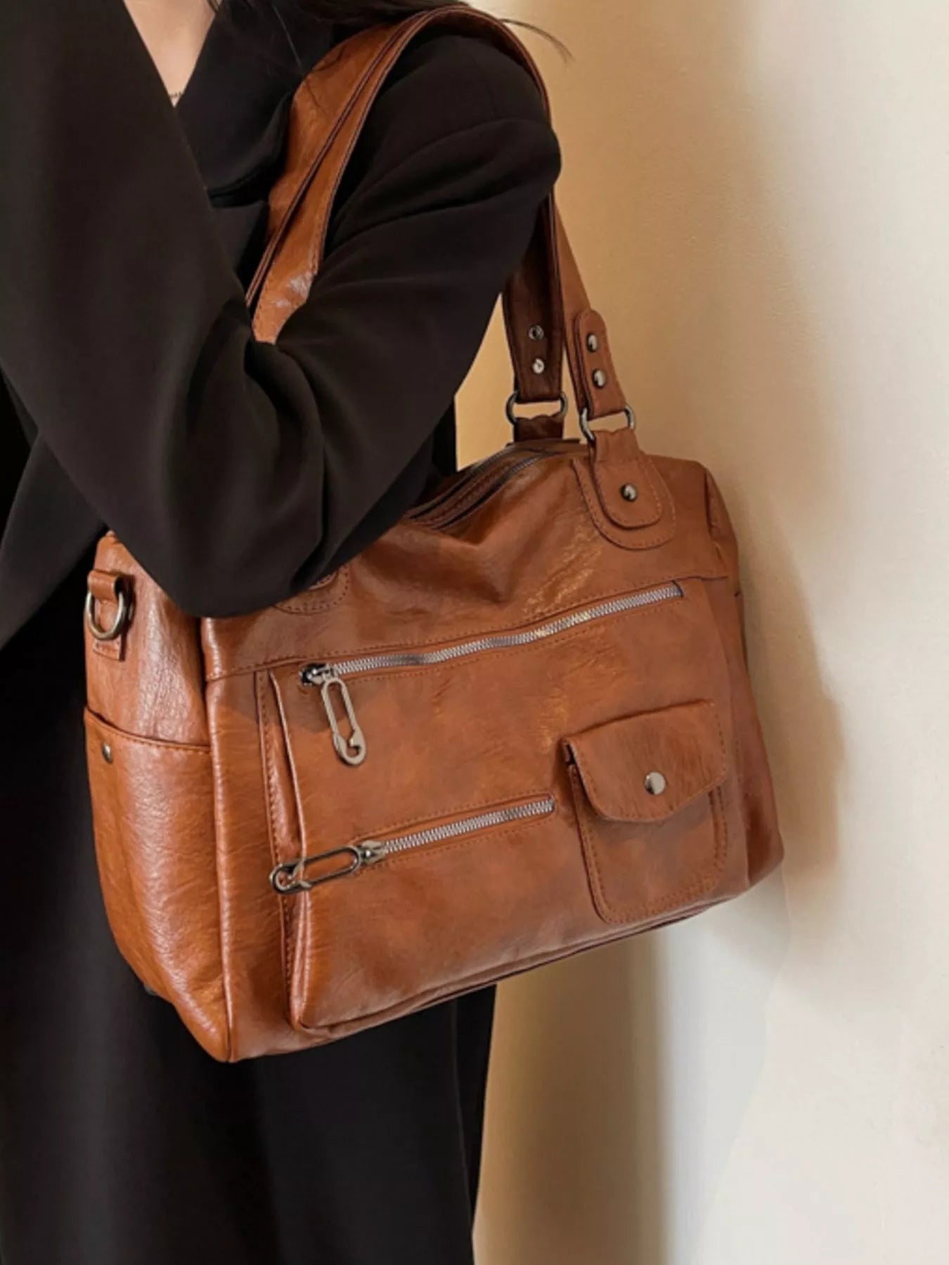 NEWYORKLISTED STYLE COLLECTION: Brown leather handbag held by a person against a neutral background