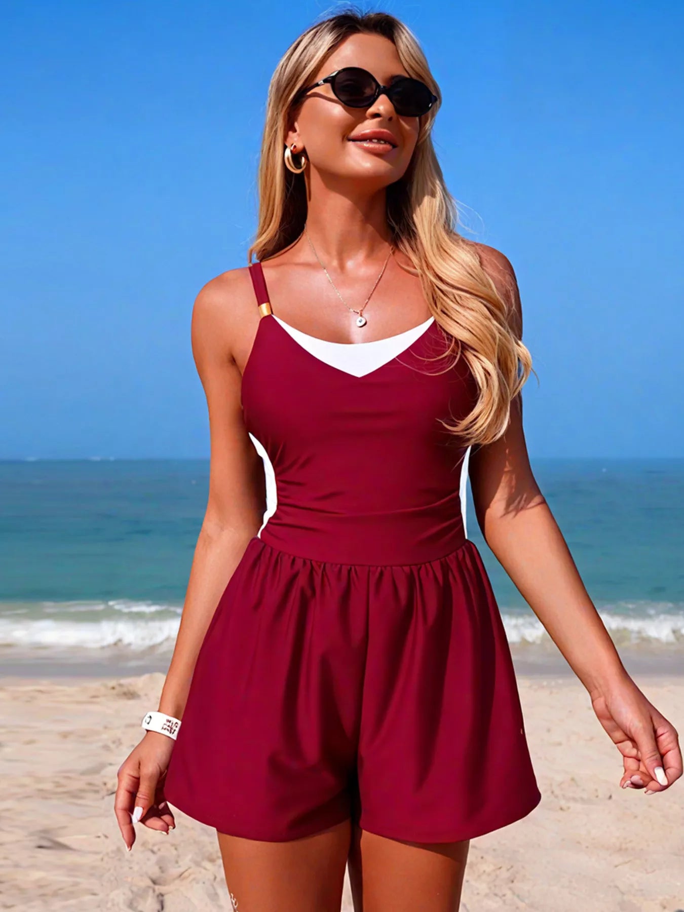 NEWYORKLISTED EDEN COLLECTION: Woman in a red romper standing on a beach with blue sky and ocean.