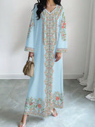 NEWYORKLISTED STYLE COLLECTION: Woman wearing a light blue dress with floral embroidery in a minimal indoor setting.