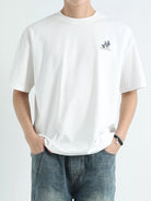 Person wearing a white t-shirt with a small logo on a plain background