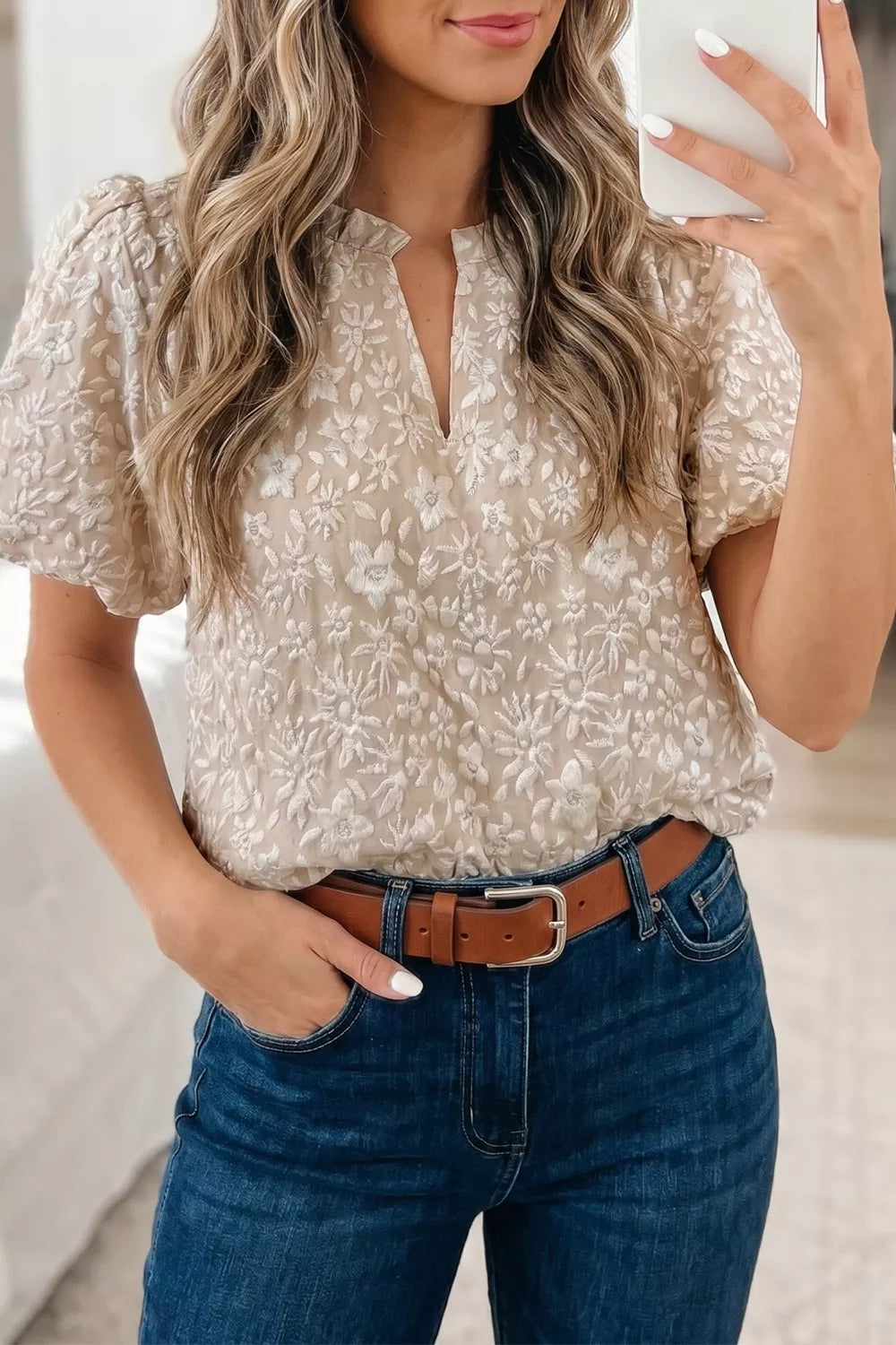 NEWYORKLISTED STYLE COLLECTION: Woman wearing a beige floral blouse and blue jeans, holding a phone.