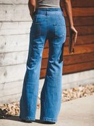 NEWYORKLISTED STYLE COLLECTION: Person wearing blue jeans standing against a wooden wall.
