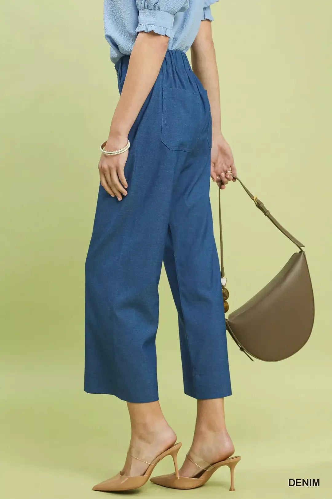 NEWYORKLISTED Style Collection: Person wearing blue pants and holding a brown handbag on a light green background