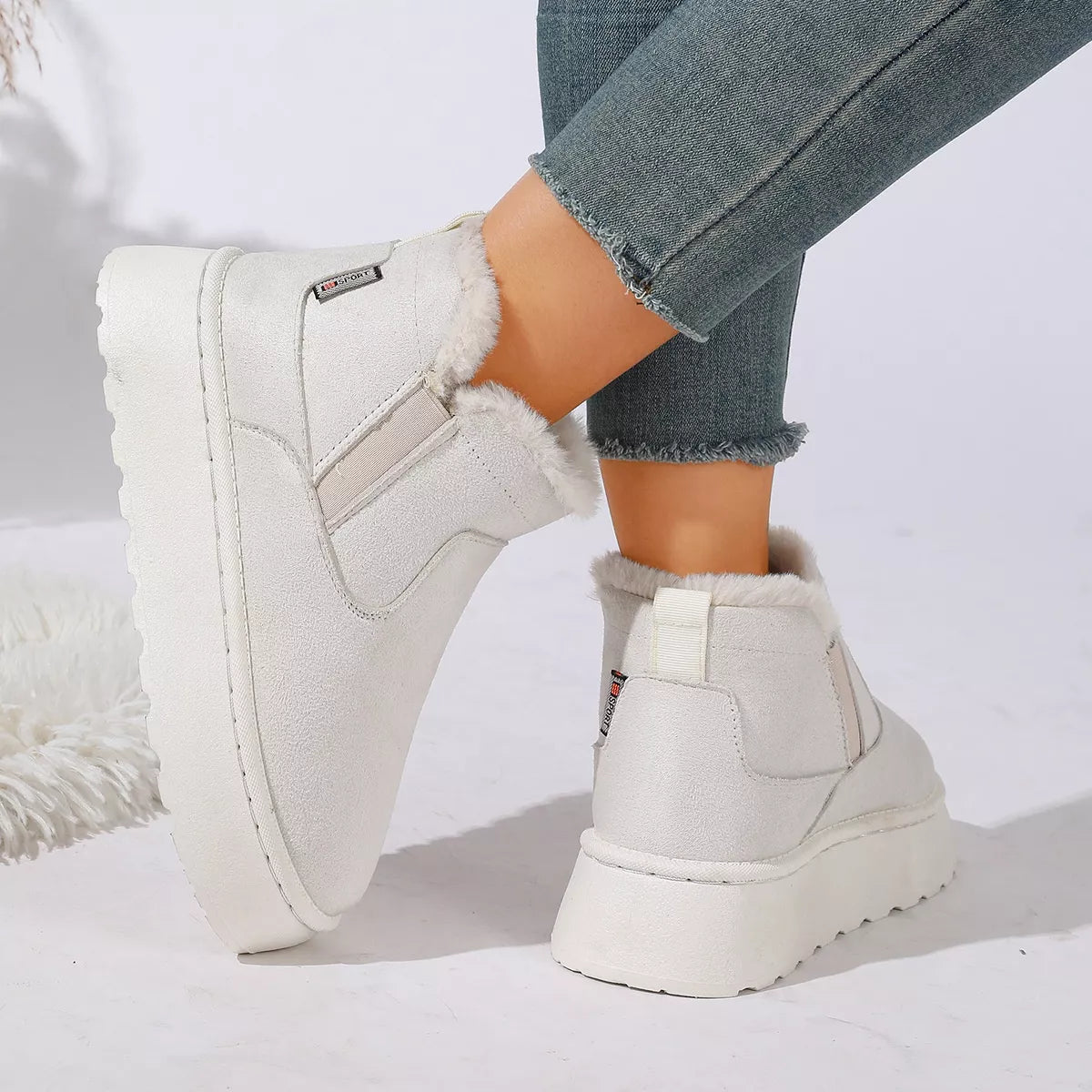 NEWYORKLISTED SHOE COLLECTION: White platform ankle boots with faux fur lining, shown on a model wearing blue jeans against a white studio background.