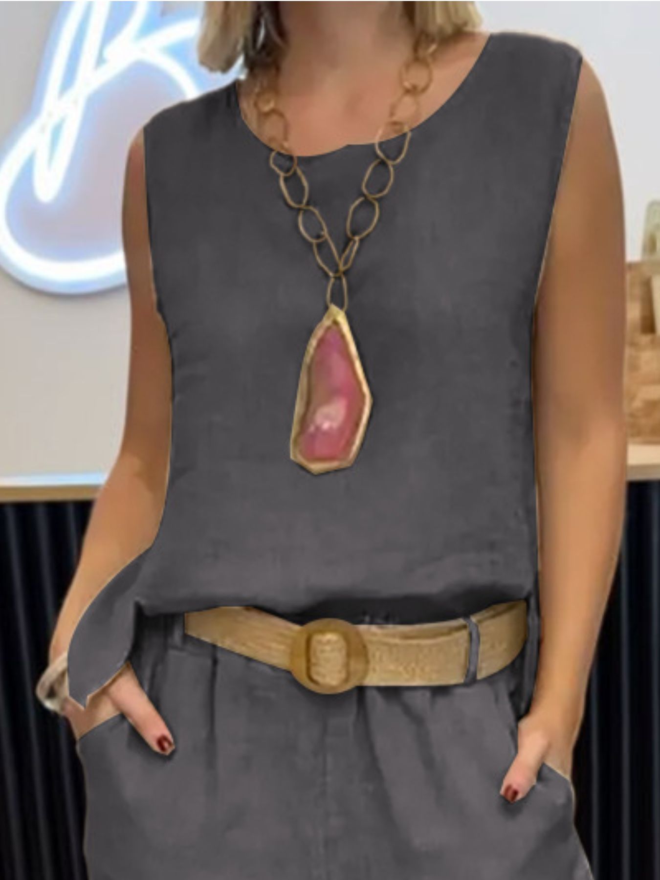 NEWYORKLISTED COMFORT COLLECTION: Person wearing a gray sleeveless top with a large necklace and belt, standing indoors.