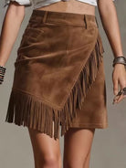 NEWYORKLISTED STYLE COLLECTION: A brown suede mini skirt with asymmetrical fringe detailing, shown on a model from the waist down against a neutral gray background.