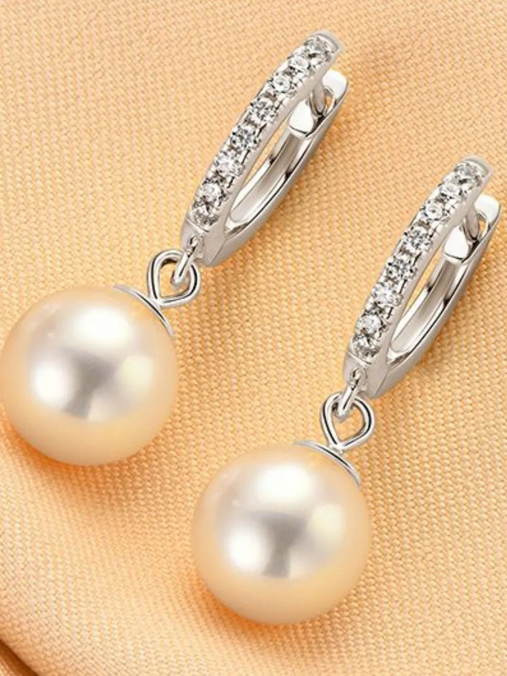 NYLD GLAMOUR COLLECTION by NEWYORKLISTED: Pearl earrings with silver hooks on a beige fabric background