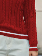 Red cable knit sweater with white stripes on a neutral background