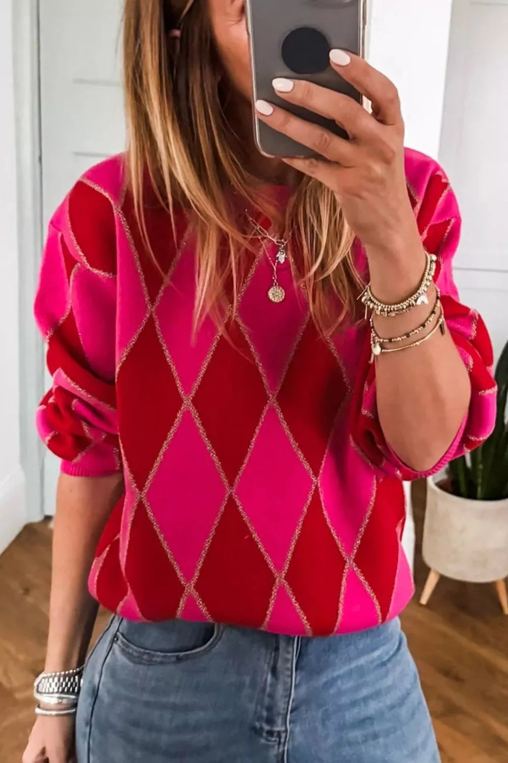 NEWYORKLISTED STYLE COLLECTION: Person wearing a pink and red argyle sweater taking a mirror selfie.