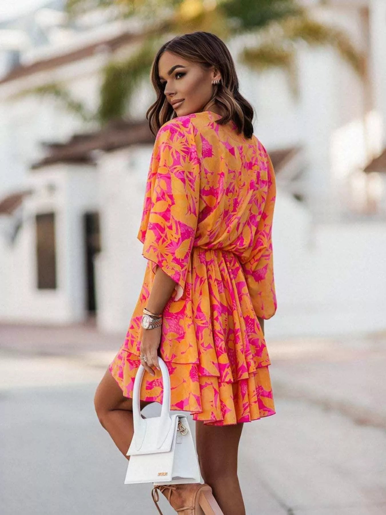 NEWYORKLISTED STYLE COLLECTION: Woman wearing a vibrant pink and orange dress with a blurred outdoor background