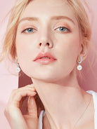 NYLD GLAMOUR COLLECTION by NEWYORKLISTED: Close-up of a person wearing pearl earrings against a pink background
