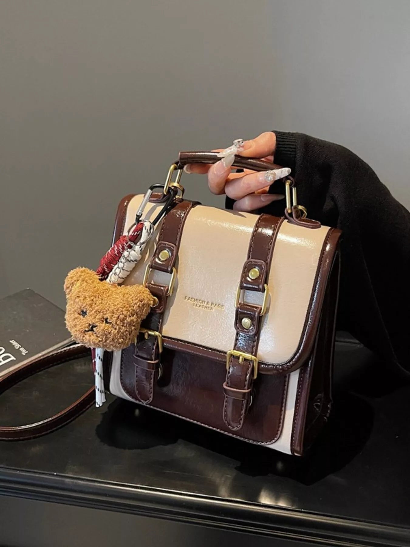 NEWYORKLISTED STYLE COLLECTION: Handbag with teddy bear charm held by a hand against a neutral background