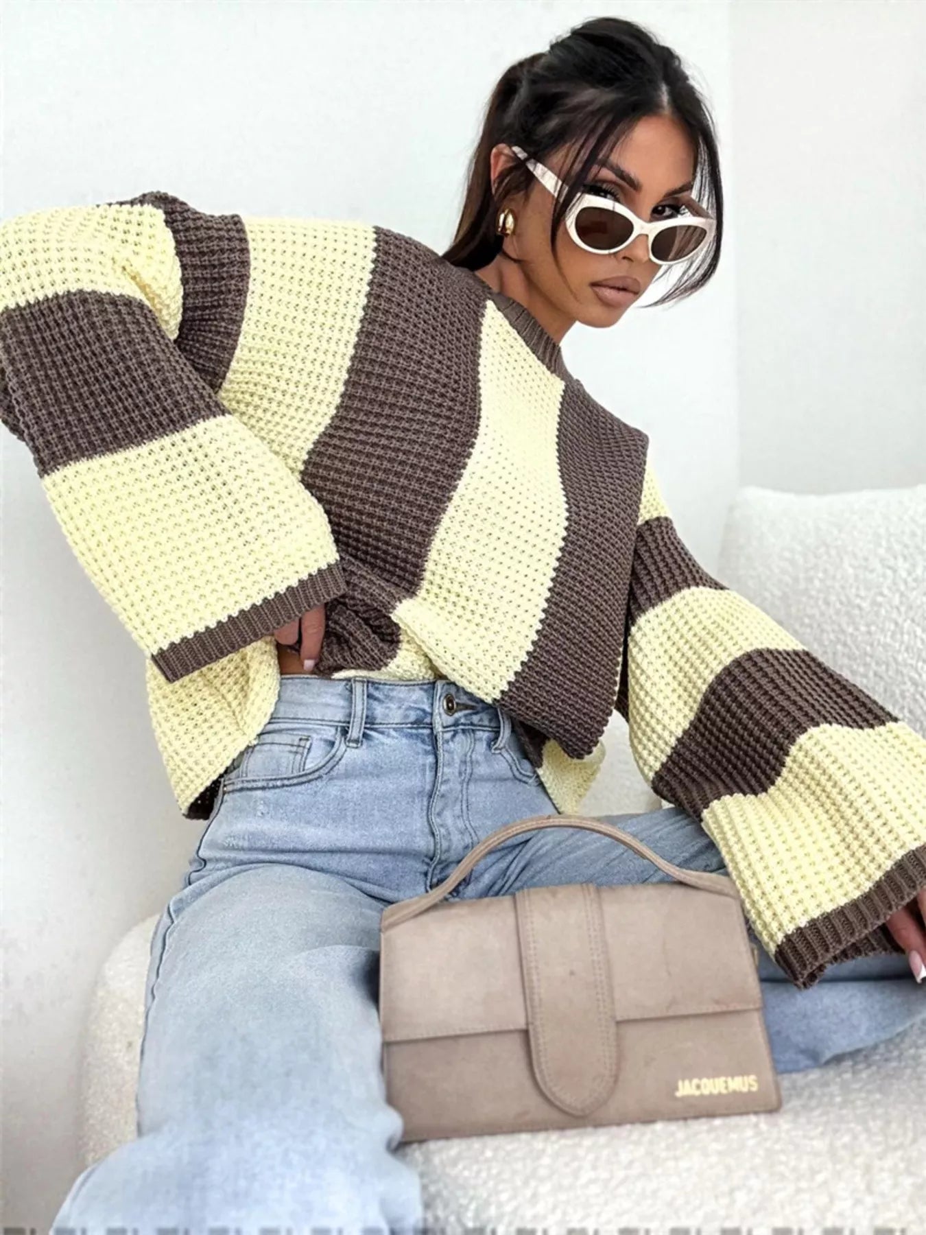 NEWYORKLISTED STYLE COLLECTION: Woman wearing a striped sweater and holding a handbag, sitting on a couch.