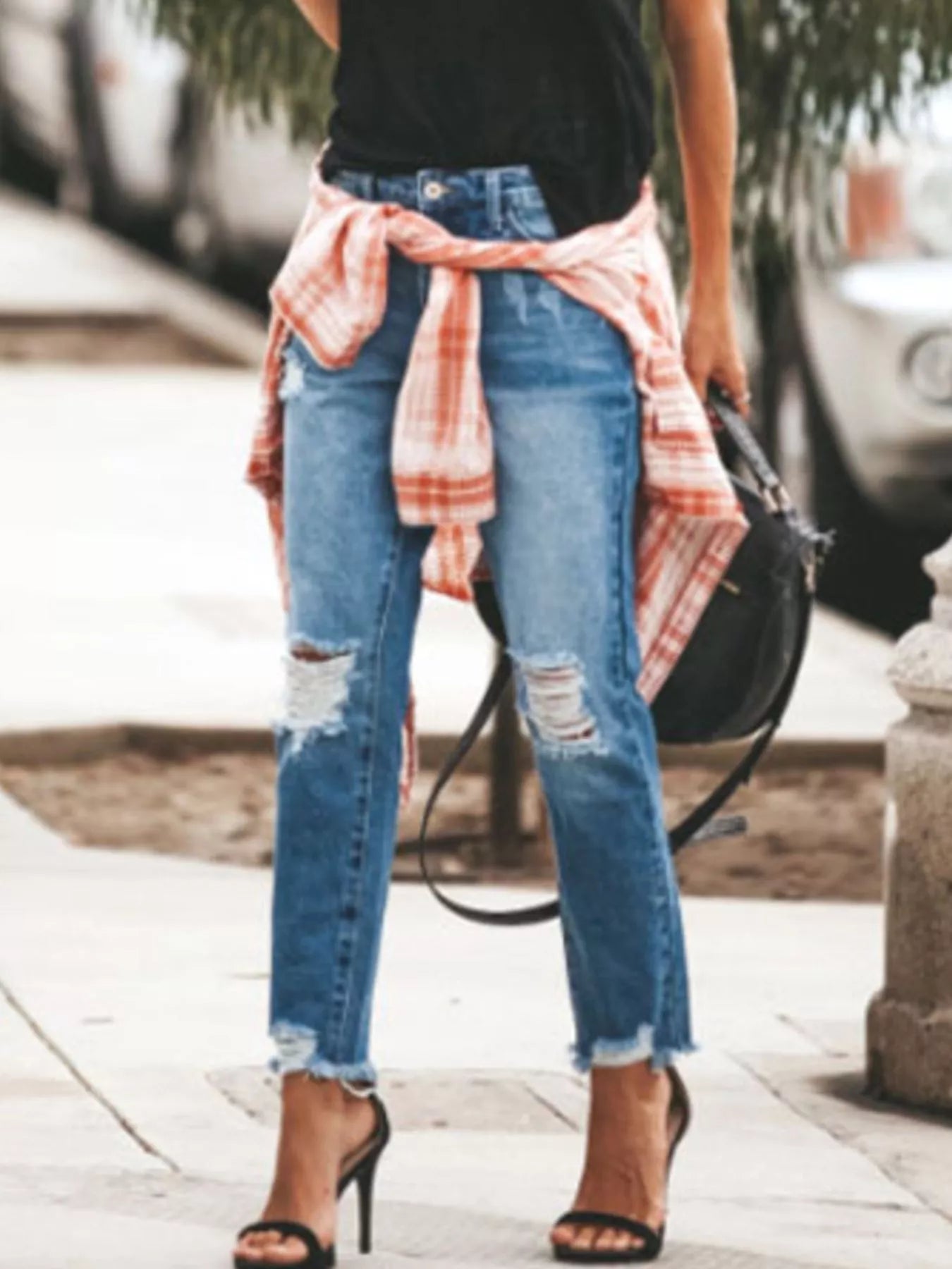 NEWYORKLISTED STYLE COLLECTION: Person wearing ripped jeans with a plaid shirt over shoulders on a sidewalk.