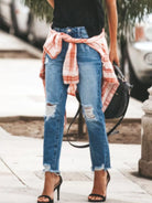 NEWYORKLISTED STYLE COLLECTION: Person wearing ripped jeans with a plaid shirt over shoulders on a sidewalk.