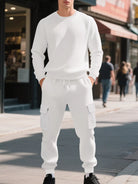 NEWYORKLISTED ATLAS MEN'S COLLECTION: A man wearing a matching white textured long-sleeve sweatshirt and cargo jogger pants stands on a city sidewalk, with blurred pedestrians and storefronts in the background.
