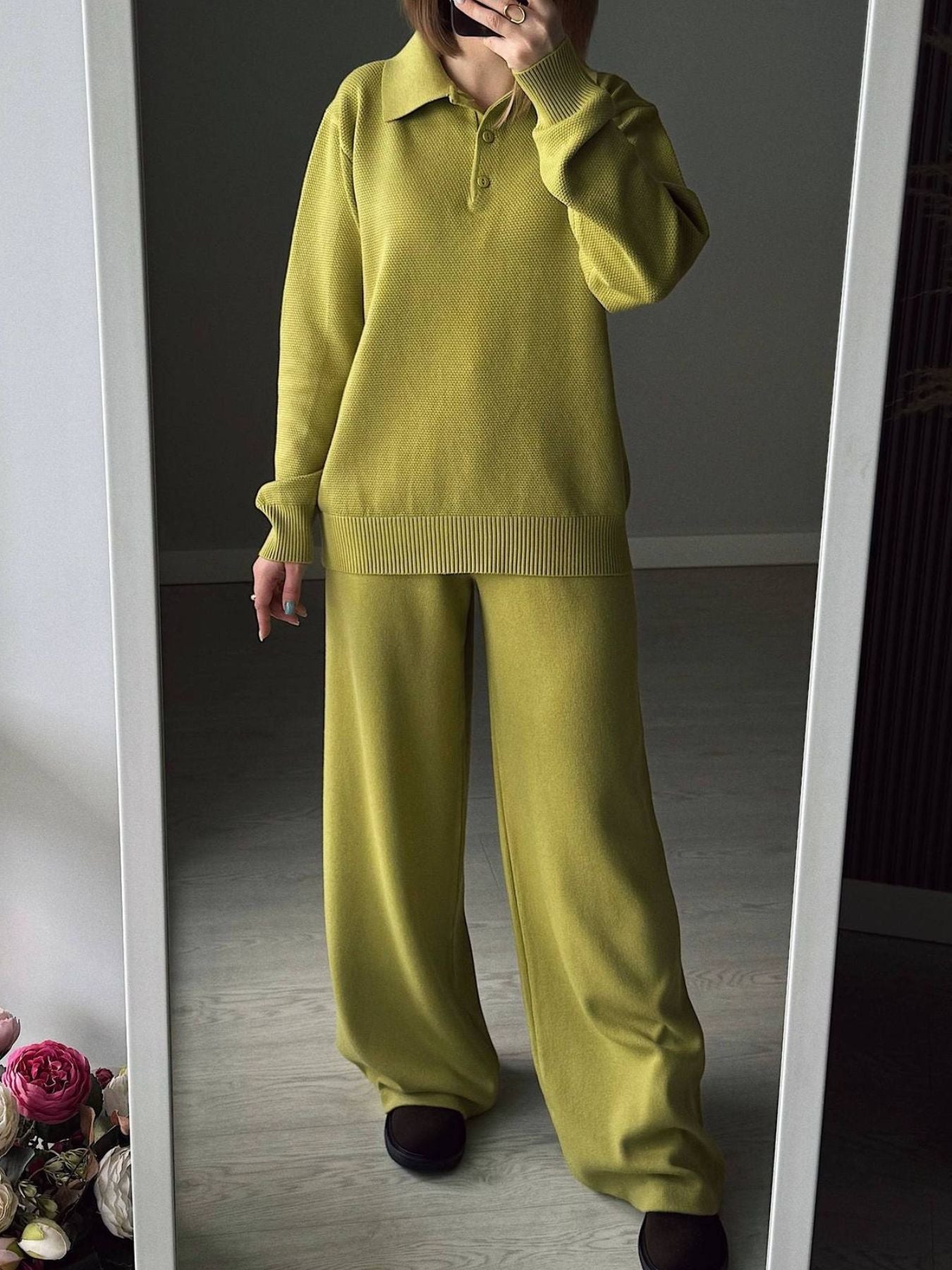 Person wearing a green sweater and pants standing in front of a mirror.