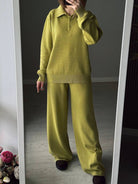 Person wearing a green sweater and pants standing in front of a mirror.