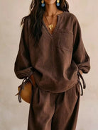 NEWYORKLISTED STYLE COLLECTION: A woman wearing a loose brown long-sleeve top and matching wide-leg pants, styled with a gold necklace, blue earrings, and a brown woven bag against a neutral beige background.