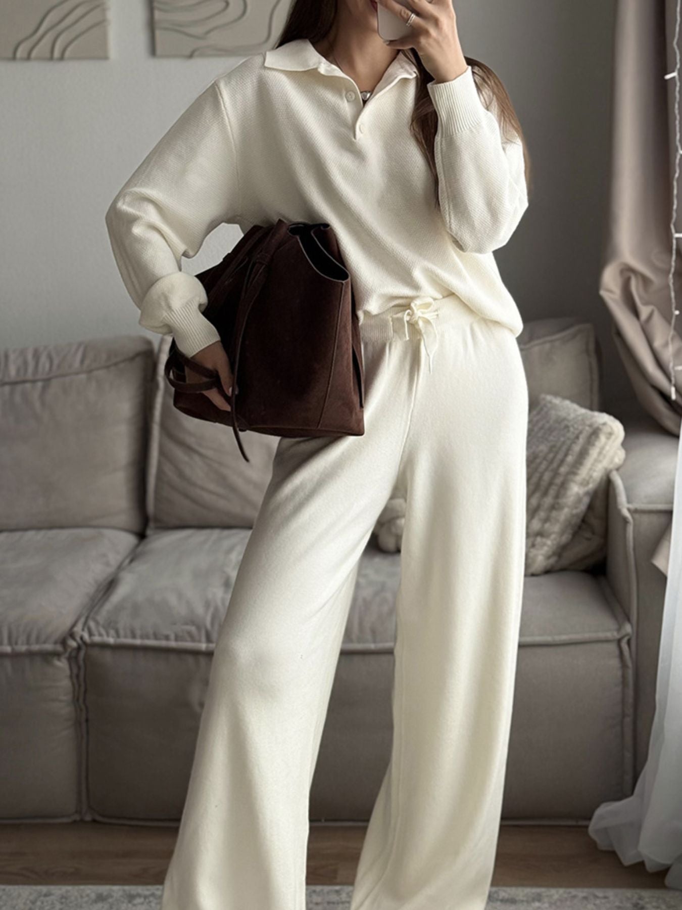 NEWYORKLISTED Comfort Collection: Person wearing a white outfit holding a brown bag in a living room.