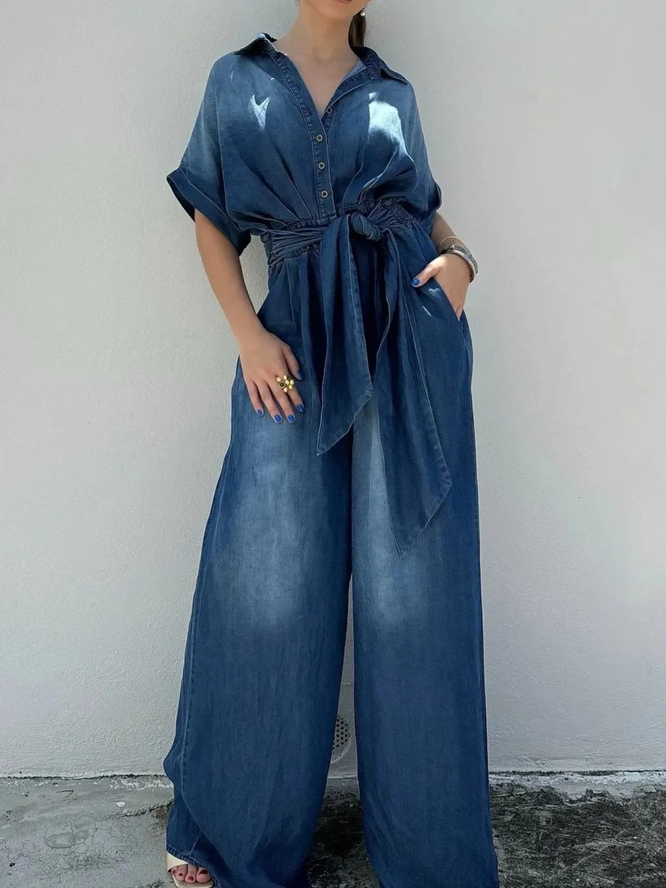 NEWYORKLISTED STYLE COLLECTION: Person wearing a blue denim jumpsuit against a plain background