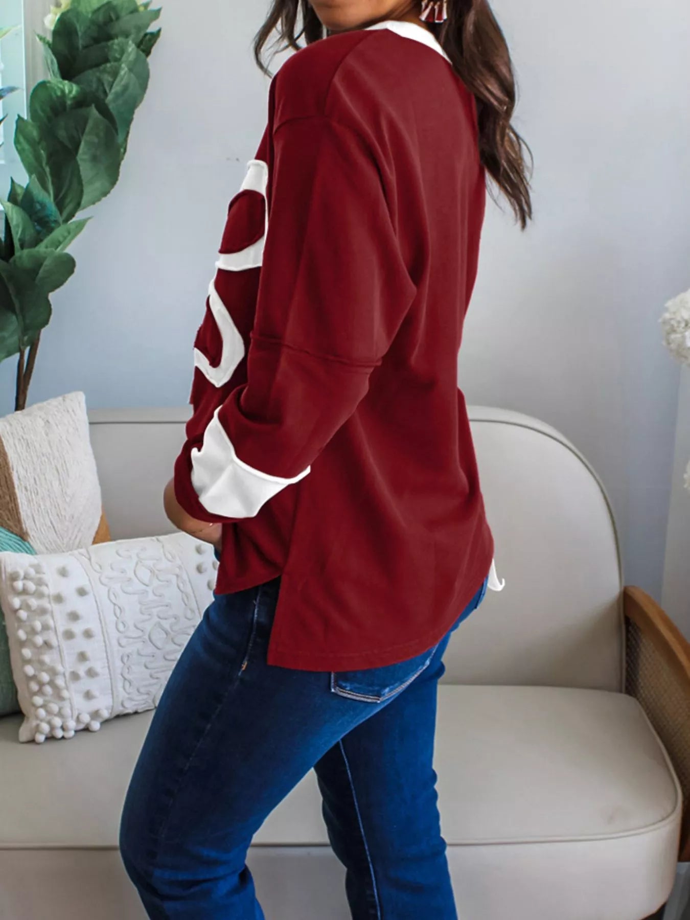 NEWYORKLISTED STYLE COLLECTION: Person wearing a red sweatshirt with white lettering in a living room setting.
